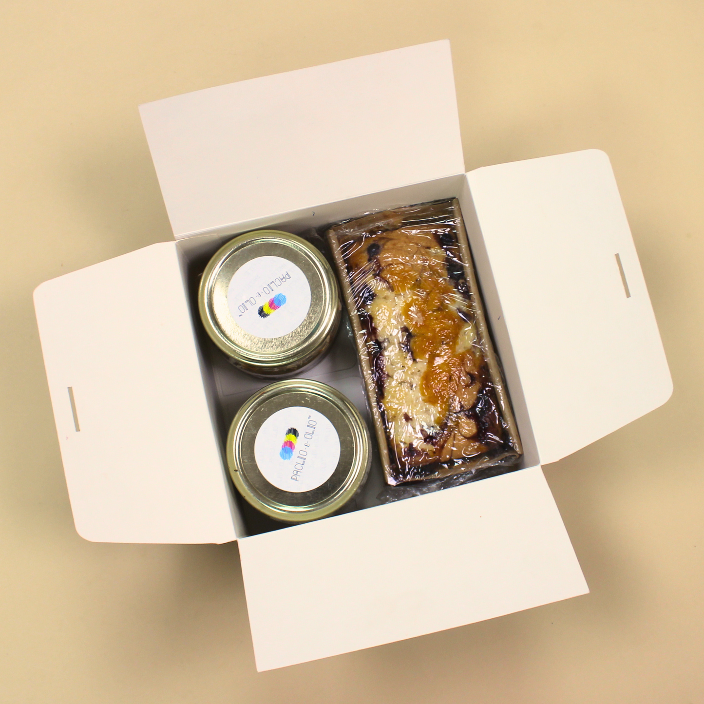 Open gift box containing two jars and a loaf of bread on a beige background